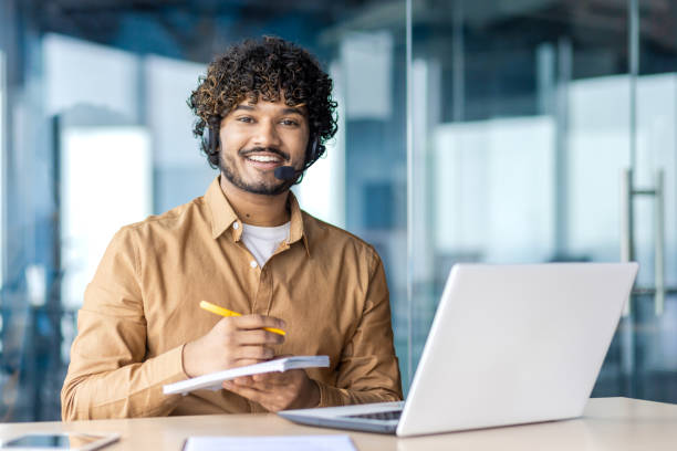 profissional masculino sorridente com fone de ouvido usando laptop no escritório moderno - multi tasking efficiency financial advisor business - fotografias e filmes do acervo