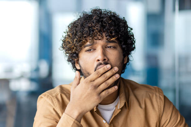 istock Young overworked and overtired businessman yawning, working inside office with laptop, boring long routine work, man in casual clothes 1972663352
