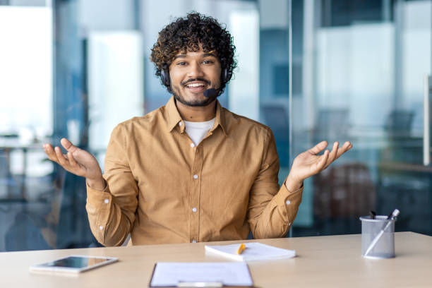 istock Web camera view, online video call, young man smiling and looking into camera with headset phone for video call, businessman inside office, selling and advising consumers, support service 1972663898