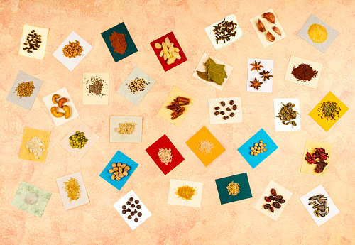 Overhead view of food ingredients over colored  labels .  The food ingredients are: brown rice, white rice, rolled oats, yellow peas, chickpeas, split peas, salt, shredded coconut, chocolate chips, sesame, slivered almonds, cashew, chia, quinoa, coffee beans, raisins, whole wheat, cinnamon stick hibiscus flower, green tea, star anise, cloves, ground coffee, black peppercorns, oregano, garlic cloves, wheat flour, garlic powder, brown sugar, birdseed, bay leaves, sunflower seeds. Image made in studio