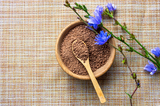 Ground chicory root in a wooden cup and chicory flowers on a rustic wooden background. Alternative medicine. Healthy drinks. chicory drink