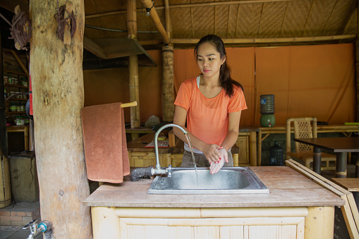 Close-up shot of Indonesian woman washing her hands in a flowing water in the sink at sustainable bamboo building