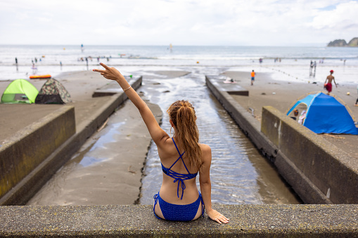 Rear view of woman in bikini sitting at beach - one hand raised