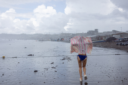 Rear view of woman in bikini running in rainy beach