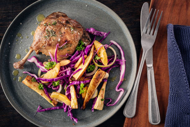 Duck confit served with a fresh sweet and sour salad of roasted parsnips with red cabbage, mandarin oranges, burnt almonds and vinaigrette dressing. High angle view, vertical format with some copy space.