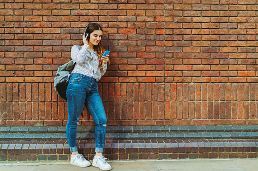 University girl listening to music against brick wall