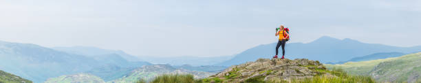 Young woman hiker standing drinking water on panoramic mountain summit