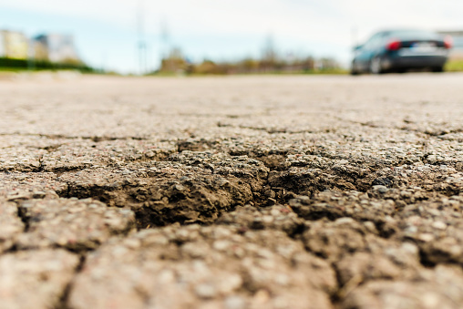 Empty damaged alphalt road in the street.Blurred blue sky,car background.