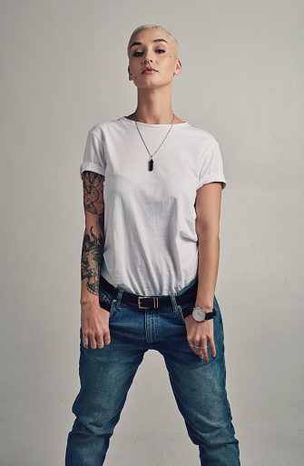 Confidence, denim and portrait of woman with tattoo fashion, creative culture and jeans in studio. Artistic girl with hipster identity, trendy style and cool clothes with pride on grey background.