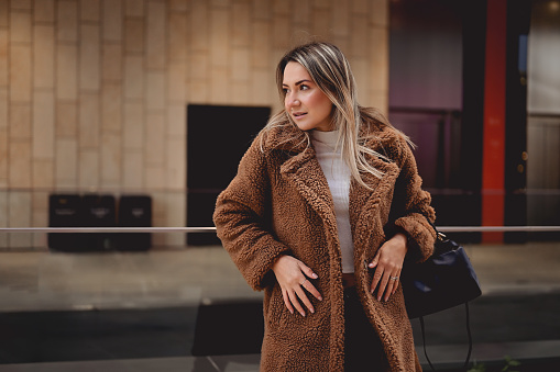 Fashionable woman in a winter teddy coat standing on a street against a wall.
