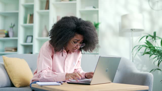 Angry african american female complains about poor performance of program on laptop sitting on sofa at home