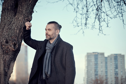 Portrait of a bearded middle-aged man in a blue coat and wool scarf against a background of high-rise buildings in the distance.