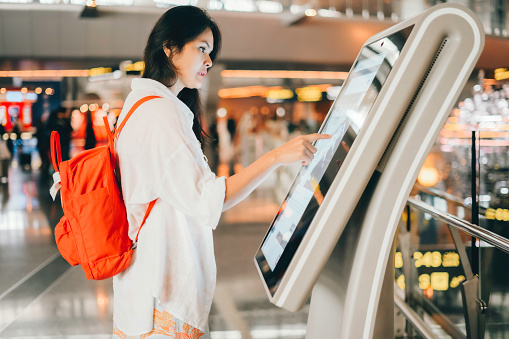 asian woman using the check in machine at the airport getting the boarding pass