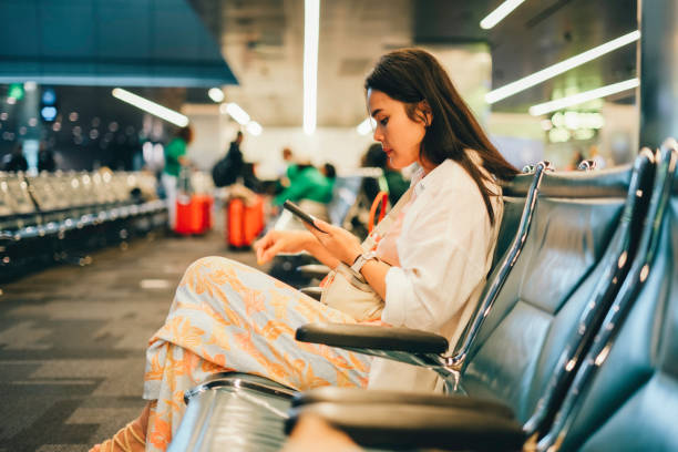 istock Young Asian woman using smartphone joyfully while waiting for night flight in airport terminal 1972744843