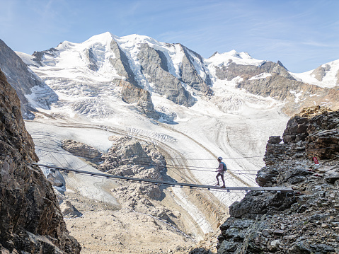 Woman on a Via Ferrata climbing route crosses suspension bridge high above glacier
