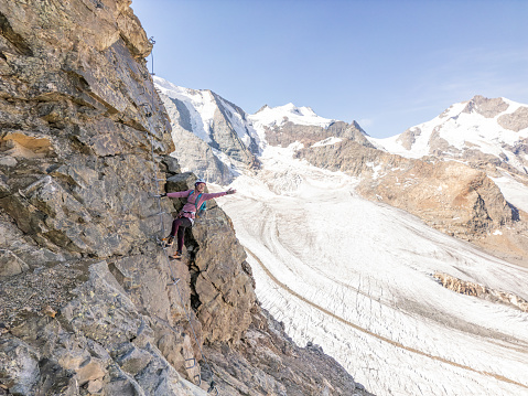 Alpine climbing in the Alps, High above spectacular glacier. Woman ascending steep rock face