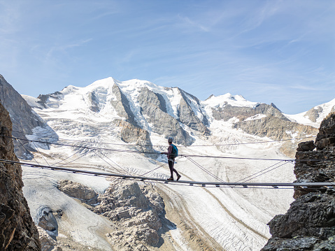 Woman on a Via Ferrata climbing route crosses suspension bridge high above glacier