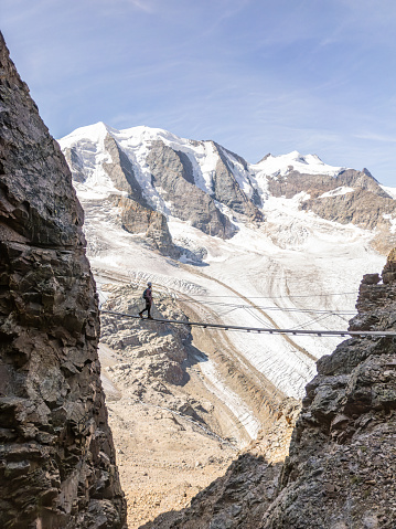 Woman on a Via Ferrata climbing route crosses suspension bridge high above glacier