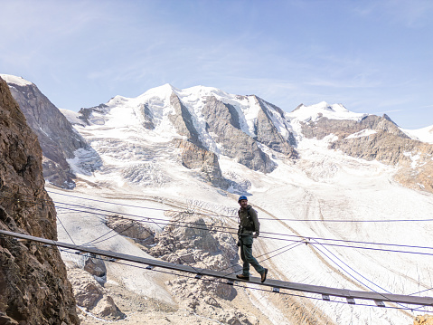 Man on a Via Ferrata climbing route crosses suspension bridge high above glacier