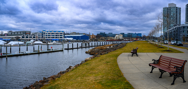 Stamford City Harbor Point Landscape with tall office and residential buildings, park benches, boardwalk footpaths, and moored boats and yachts at the dock on a dramatic stormy winter in Connecticut, USA