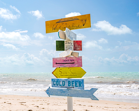 A colourful, wooden signpost, on a tropical beach, against a blue, summer sky