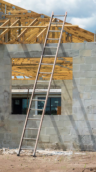 Tall ladder leaning against the concrete shell of a single-family house under construction in a suburban development on a cloudy day in southwest Florida