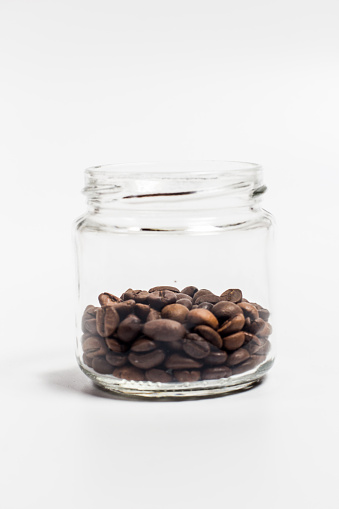 Fragrant coffee grains in a small glass jar on a white background