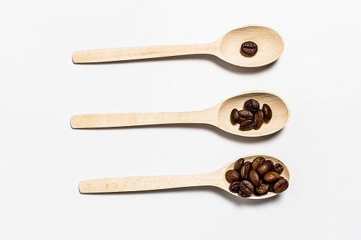 Fragrant coffee grains in light wooden spoons on a white background