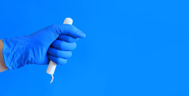 tampón en un aplicador de cartón en la mano de una mujer, fondo azul - tampon menstruation applicator hygiene fotografías e imágenes de stock