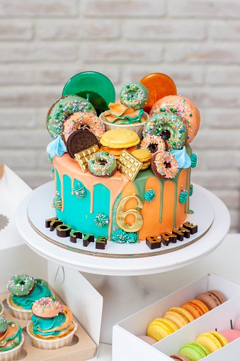 Delicious two-sided birthday cake made in green and orange colors richly decorated with donuts and lollipops. Celebrating two birthdays at once.
