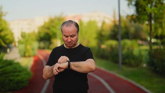 A senior runner sportsman is excising and checking his smart watch outdoors.