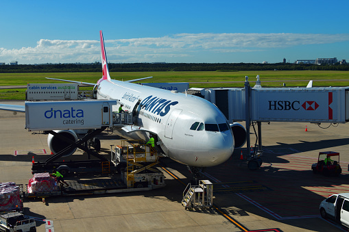 Brisbane, Queensland, Australia: Qantas Airbus A330-303, registration VH-QPG, MSN 603, named Mount Gambier - at a passenger boarding bridge (with HSBC ad), being serviced by Dnata Catering and Cabin Services Australia vehicles - Brisbane Airport (BNE).