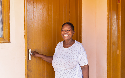 village african old woman, with braids hairstyle , standing in front of the house holding the door handle