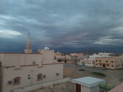 A mosque with a minaret in the middle of residential houses in a small city on a winter day and a sky full of clouds at sunset