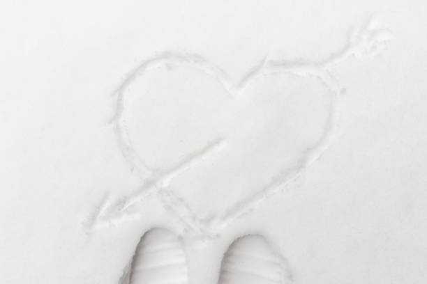 Single drawn heart pierced by an arrow in the snow, top view.