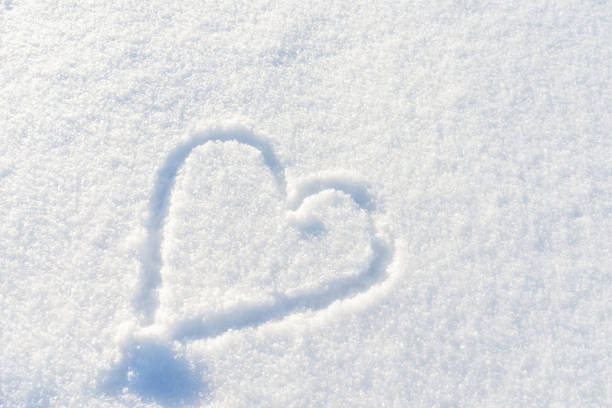 POV of woman standing in snow with heart shape drawn on the ground. Woman enjoying winter concept.