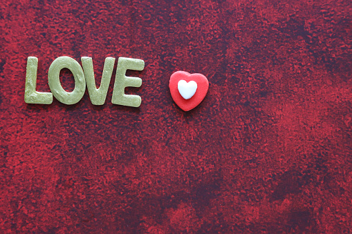 Stock photo showing elevated view of mottled red-black background with gold 'love' lettering, Valentine's Day greeting card sign with red and white icing candy heart.