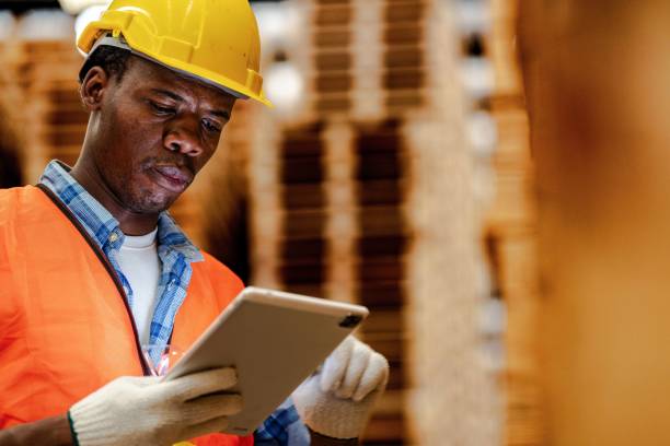 istock African worker carpenter wearing safety uniform and hard hat working and checking the quality of wooden products at workshop manufacturing. man and woman workers wood in dark warehouse industry. 1972839441