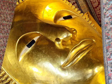 Close up Ancient Face of Golden Reclining Buddha Image at Wat Pho Temple where is a Famous Temple and Historical Landmark of Bangkok Thailand, that Located beside Temple of the Emerald Buddha.