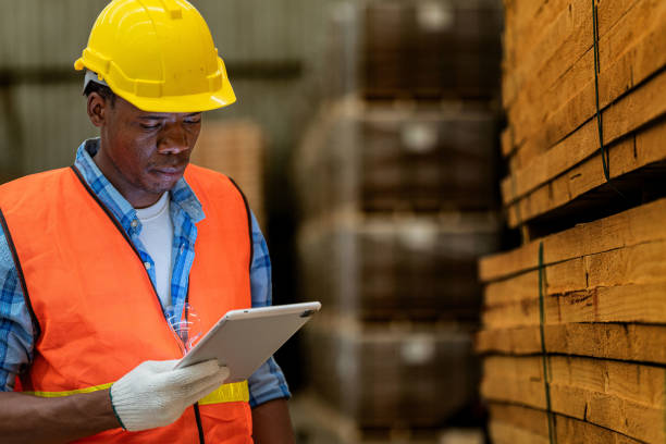 istock African worker carpenter wearing safety uniform and hard hat working and checking the quality of wooden products at workshop manufacturing. man and woman workers wood in dark warehouse industry. 1972841628