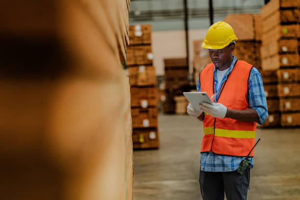 istock African worker carpenter wearing safety uniform and hard hat working and checking the quality of wooden products at workshop manufacturing. man and woman workers wood in dark warehouse industry. 1972842166