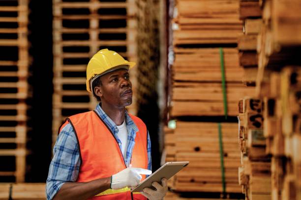istock African worker carpenter wearing safety uniform and hard hat working and checking the quality of wooden products at workshop manufacturing. man and woman workers wood in dark warehouse industry. 1972846394