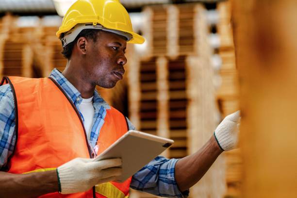 istock African worker carpenter wearing safety uniform and hard hat working and checking the quality of wooden products at workshop manufacturing. man and woman workers wood in dark warehouse industry. 1972847992