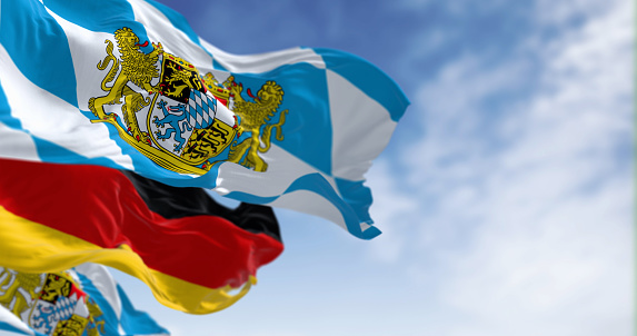 Bavarian flags waving with national german flag on a clear day. Bavaria is a state in the south-east of Germany. 3d illustration render. Selective focus. Fluttering fabric.