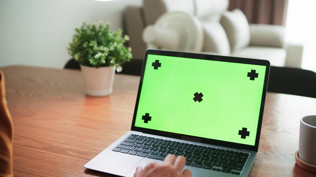 Closeup of young Asian woman using laptop with mock-up green screen while working in living room at home
