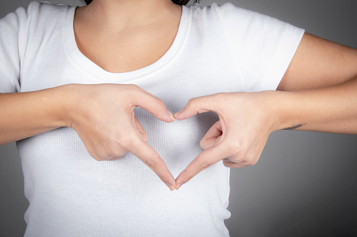 Young caucasian woman in white t-shirt showing love gesture near heart