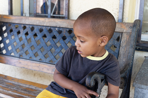 mixed race african toddler with shaved head playing on an forged iron bench in front of the house