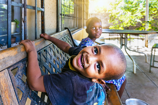 mixed race boy resting on an forged iron bench in front of the house in the favela, playing with his sister