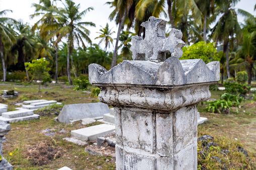 Gray gravestone with cross on top mounted at La Digue cemetery, Seychelles