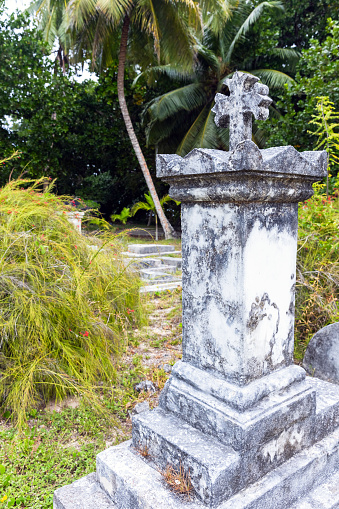 Gray gravestone with cross on top mounted at La Digue cemetery, Seychelles. Vertical photo